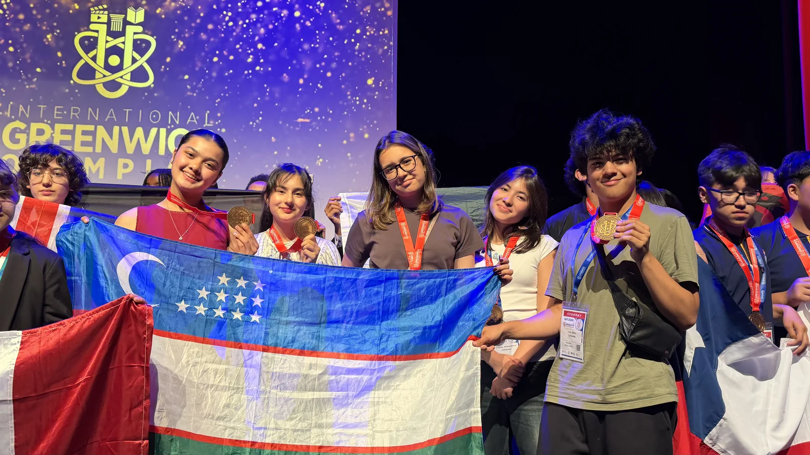 CST students on stage holding medals and the flag of Uzbekistan